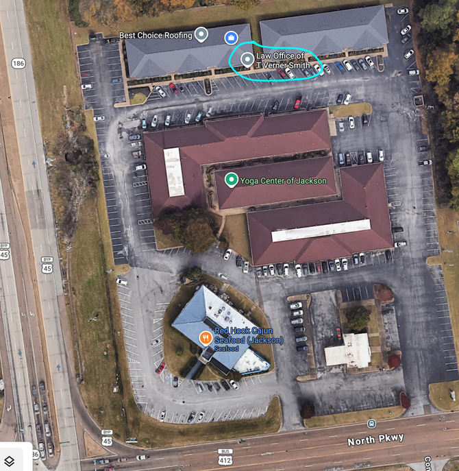 Aerial view of a building complex with parking lots, roads, and colored map markers.