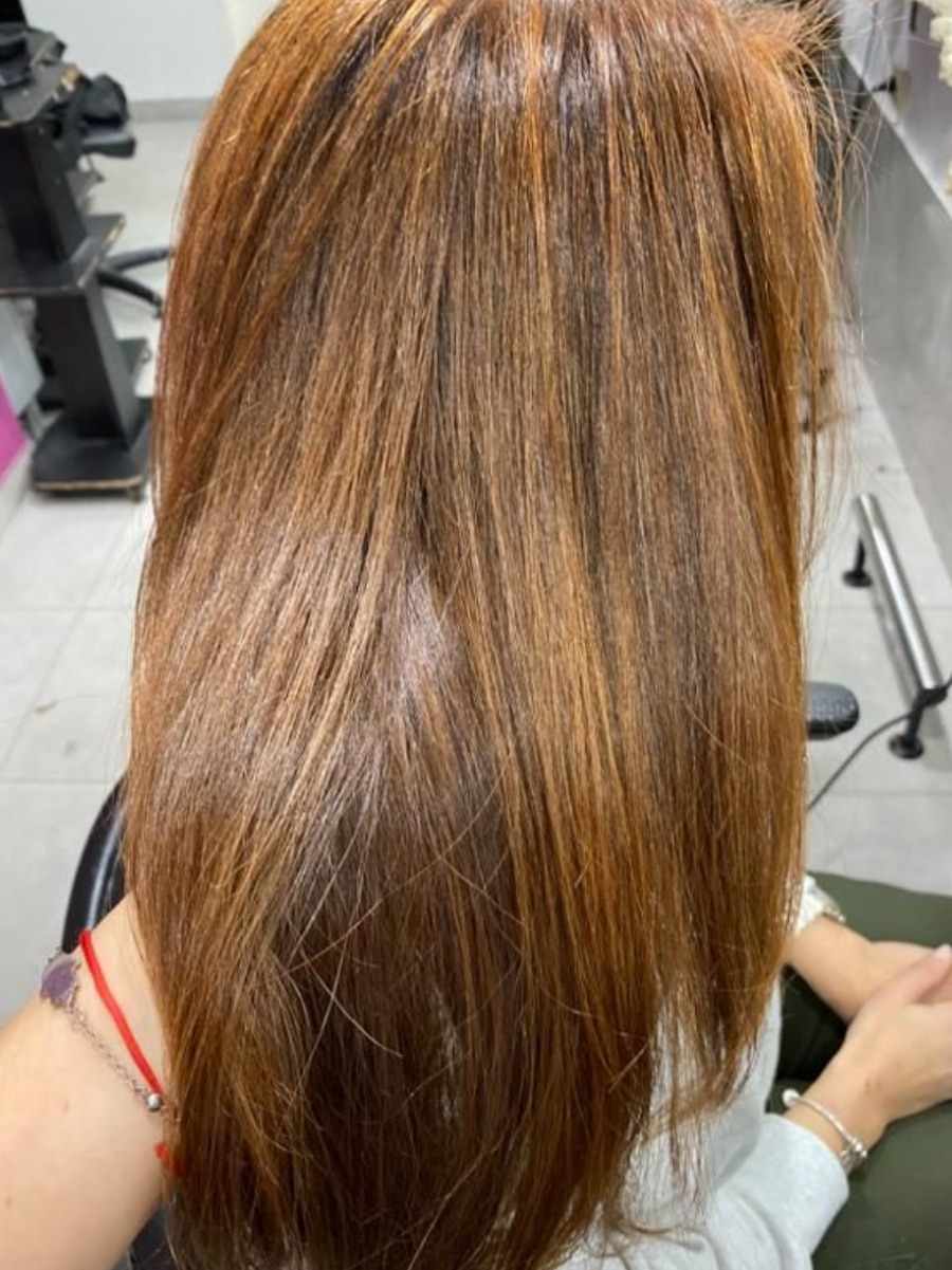 Mujer con cabello largo castaño rojizo y reflejos dorados en un salón de belleza.