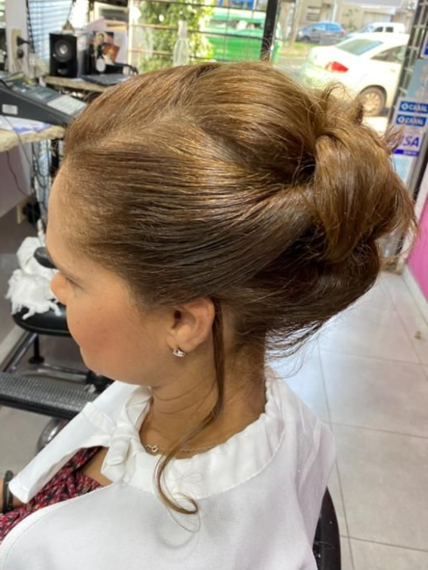 Mujer con cabello castaño peinado hacia atrás, sentada en un salón.