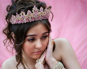 Mujer joven que lleva una tiara con joyas de color rosa, apoyando la barbilla sobre sus manos; fondo rosa.