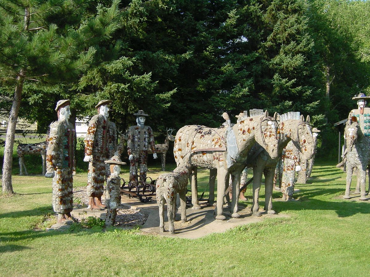 People in camouflage standing beside a stone elephant sculpture in a grassy park