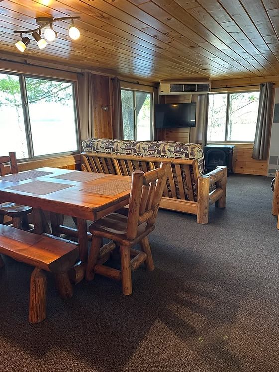 Log cabin dining area with wooden furniture, including a table, bench, and chairs, and a couch.