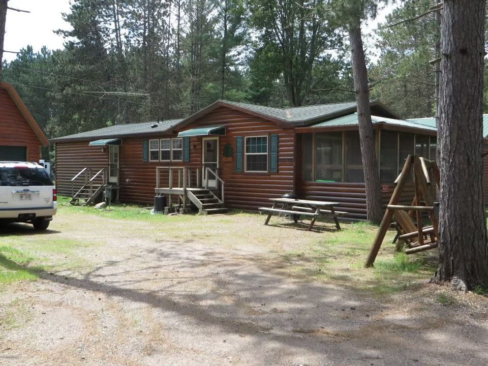 Log cabin with a screened porch, picnic table, and swing set; parked vehicle.