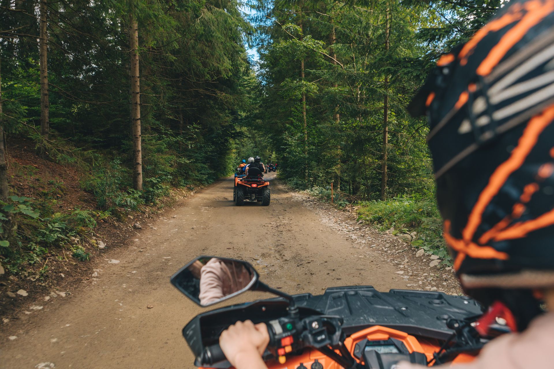 First-person view of an ATV ride on a dirt forest trail, following another rider ahead