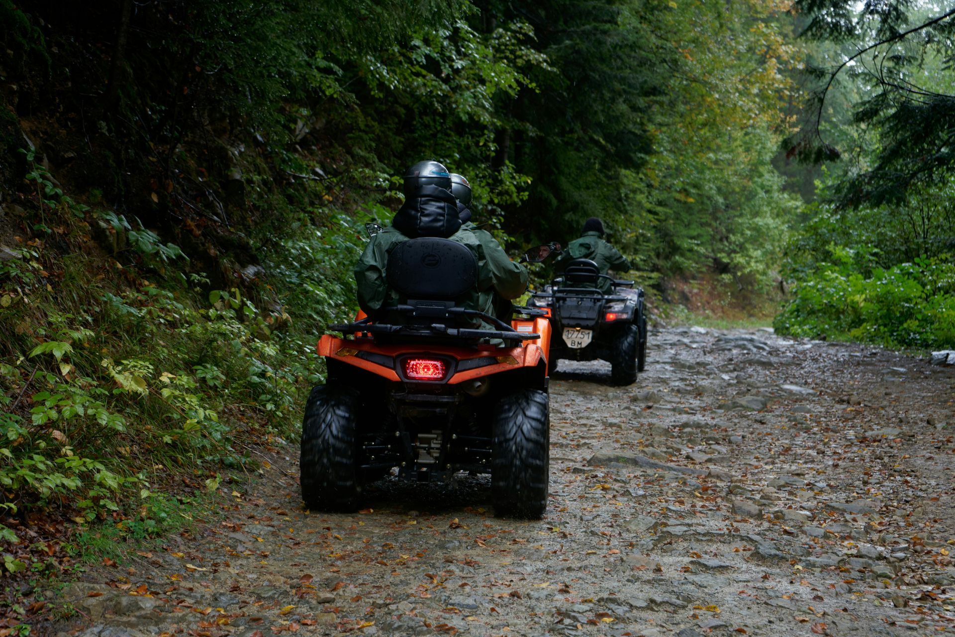 Two people riding ATVs on a muddy forest path.
