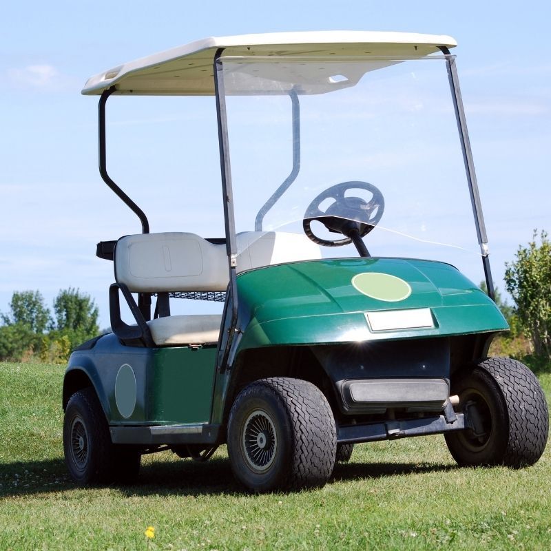 Green golf cart parked on grass under a blue sky