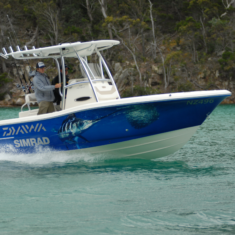 Blue fishing boat with a person onboard on turquoise water near a rocky shoreline