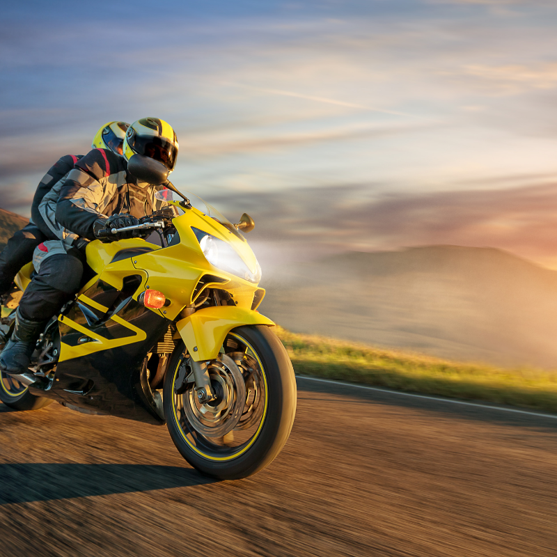 Yellow sport motorcycle racing on a road at sunset, rider leaning into a turn