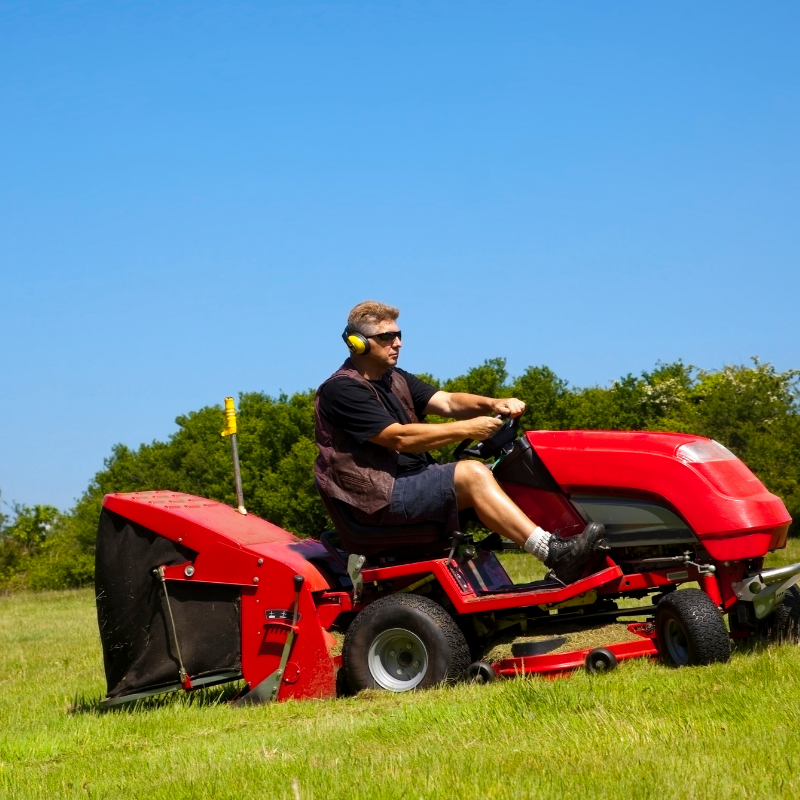 Man riding a red lawn mower on a grassy field under a blue sky