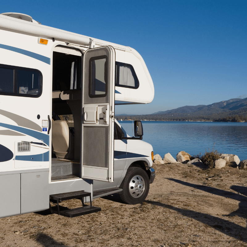 White RV parked by a lakeshore with the door open on a clear day