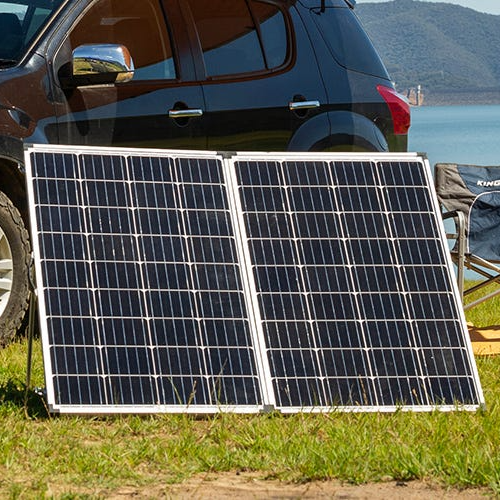Portable solar panels leaning against a black SUV by a lakeside campsite
