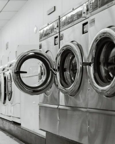 A black and white photo of a row of washing machines in a laundromat.