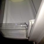 The inside of an empty refrigerator with the door open and the side of the rack is broken.