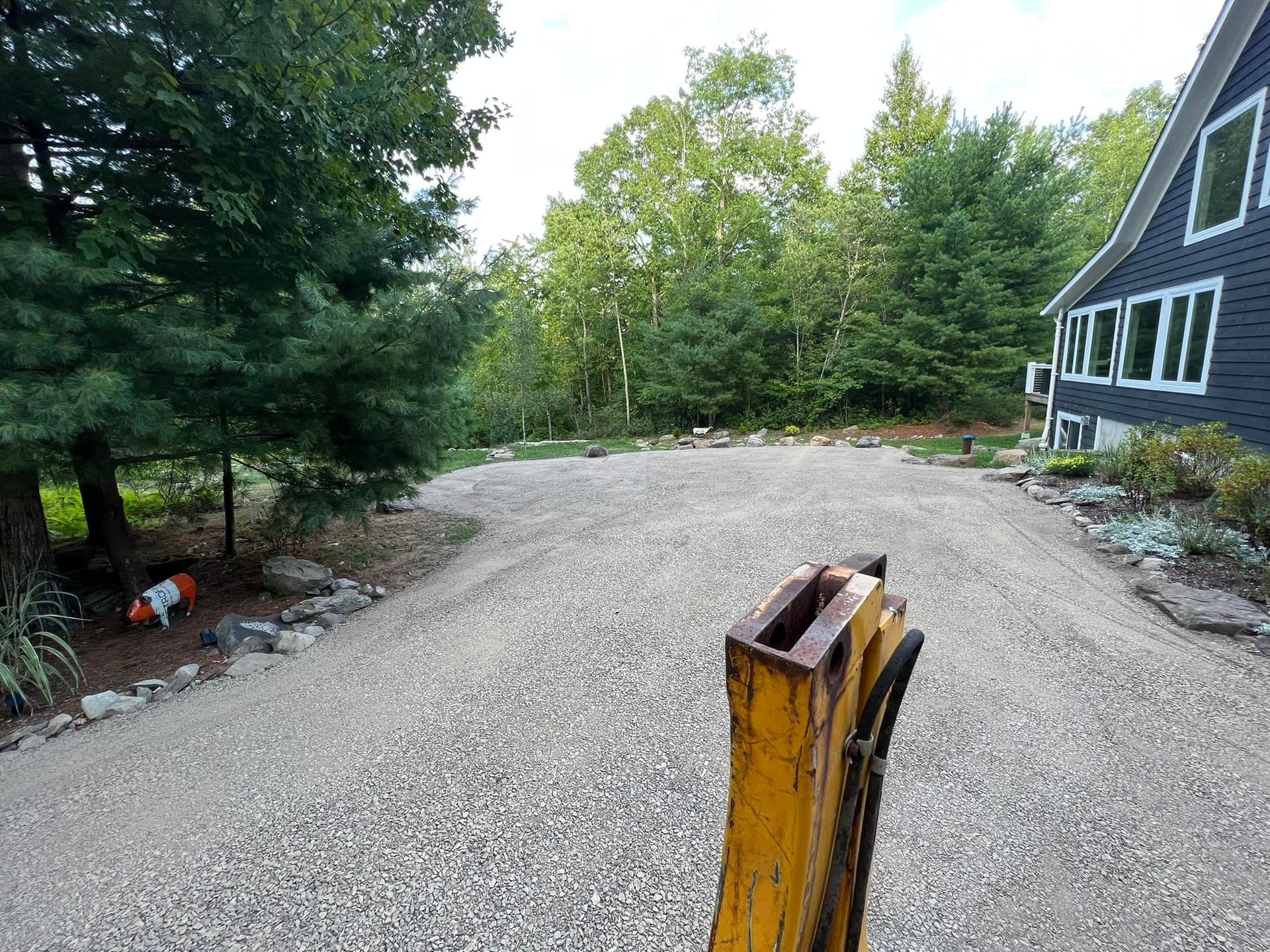 A yellow pole is in the middle of a gravel road in front of a house.