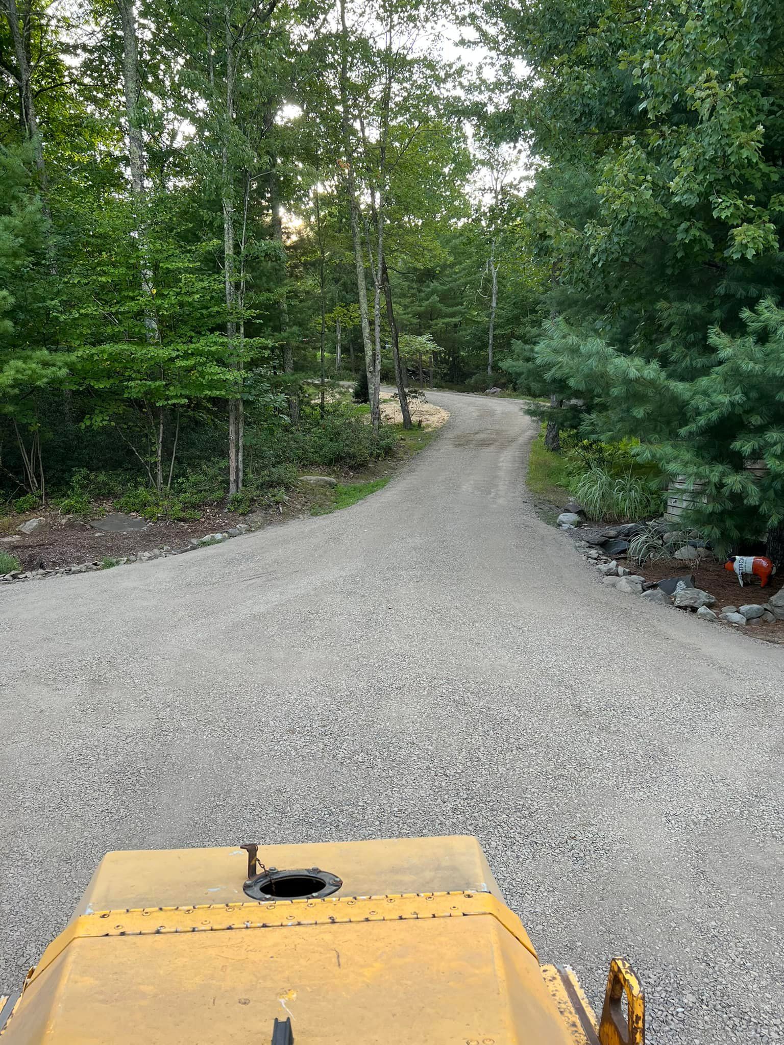 A yellow tractor is driving down a gravel road in the woods.