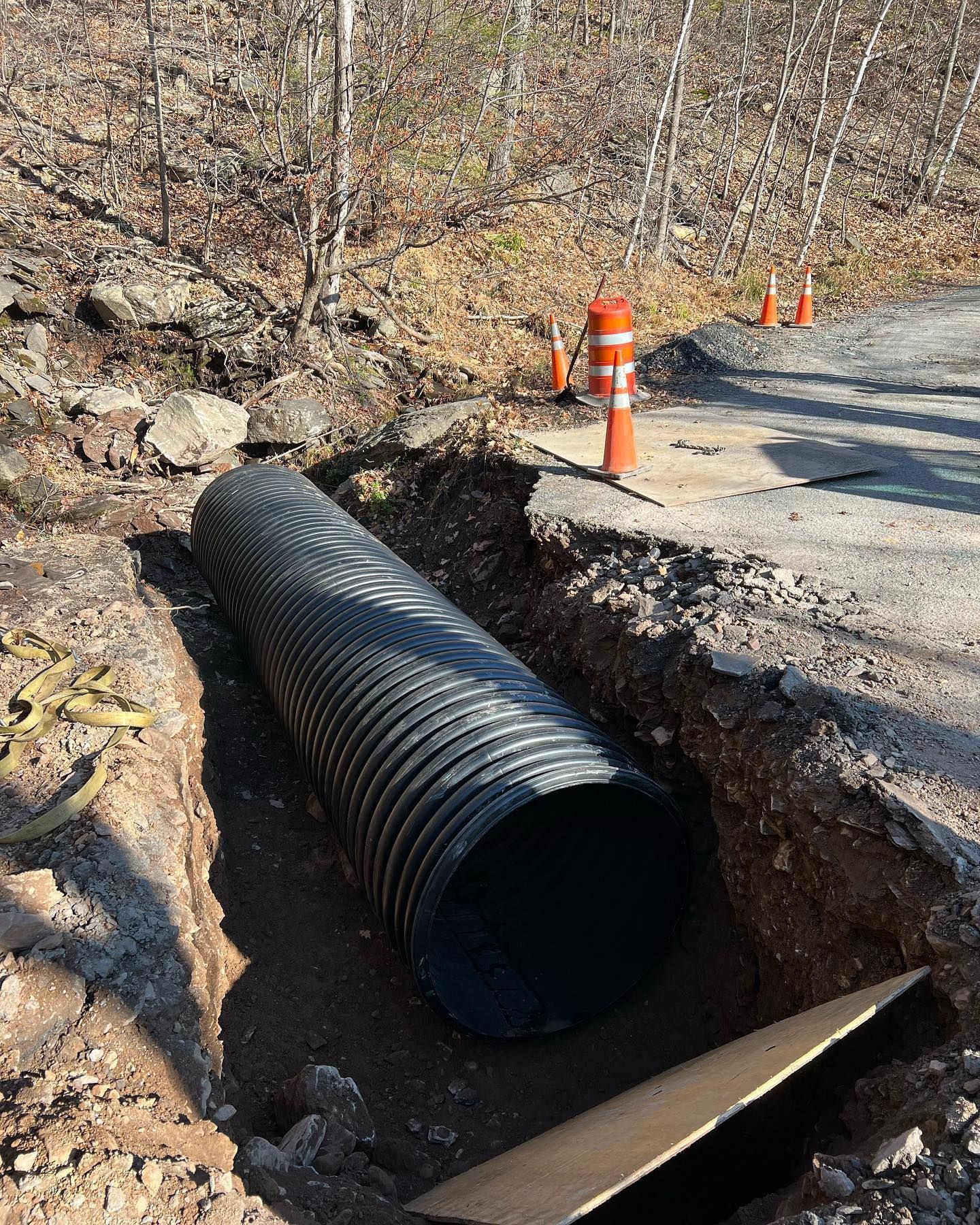 A large black pipe is sitting in the dirt next to a road.