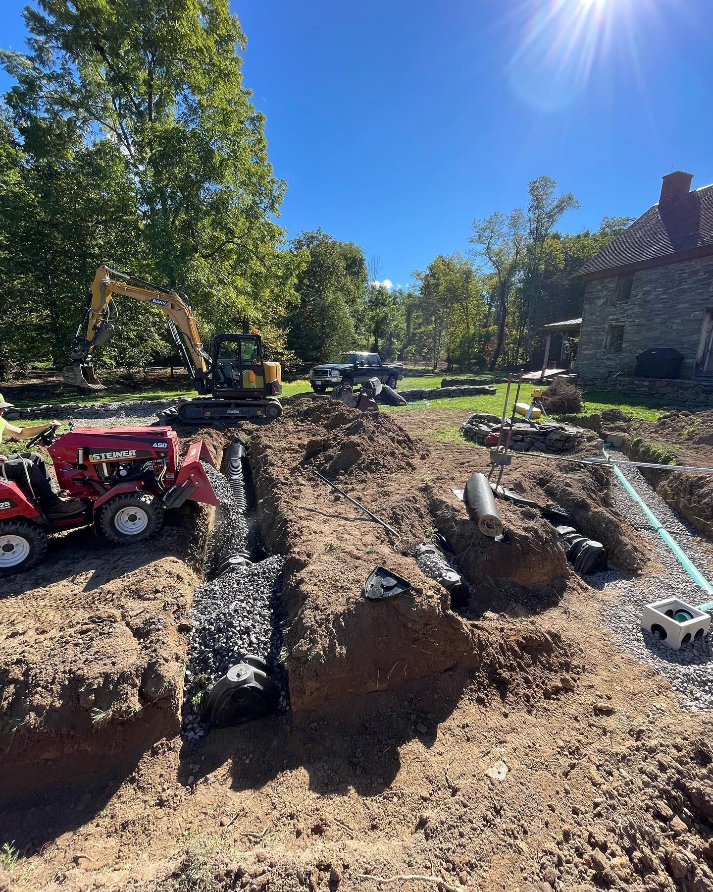 A tractor is digging a hole in the dirt in front of a house.