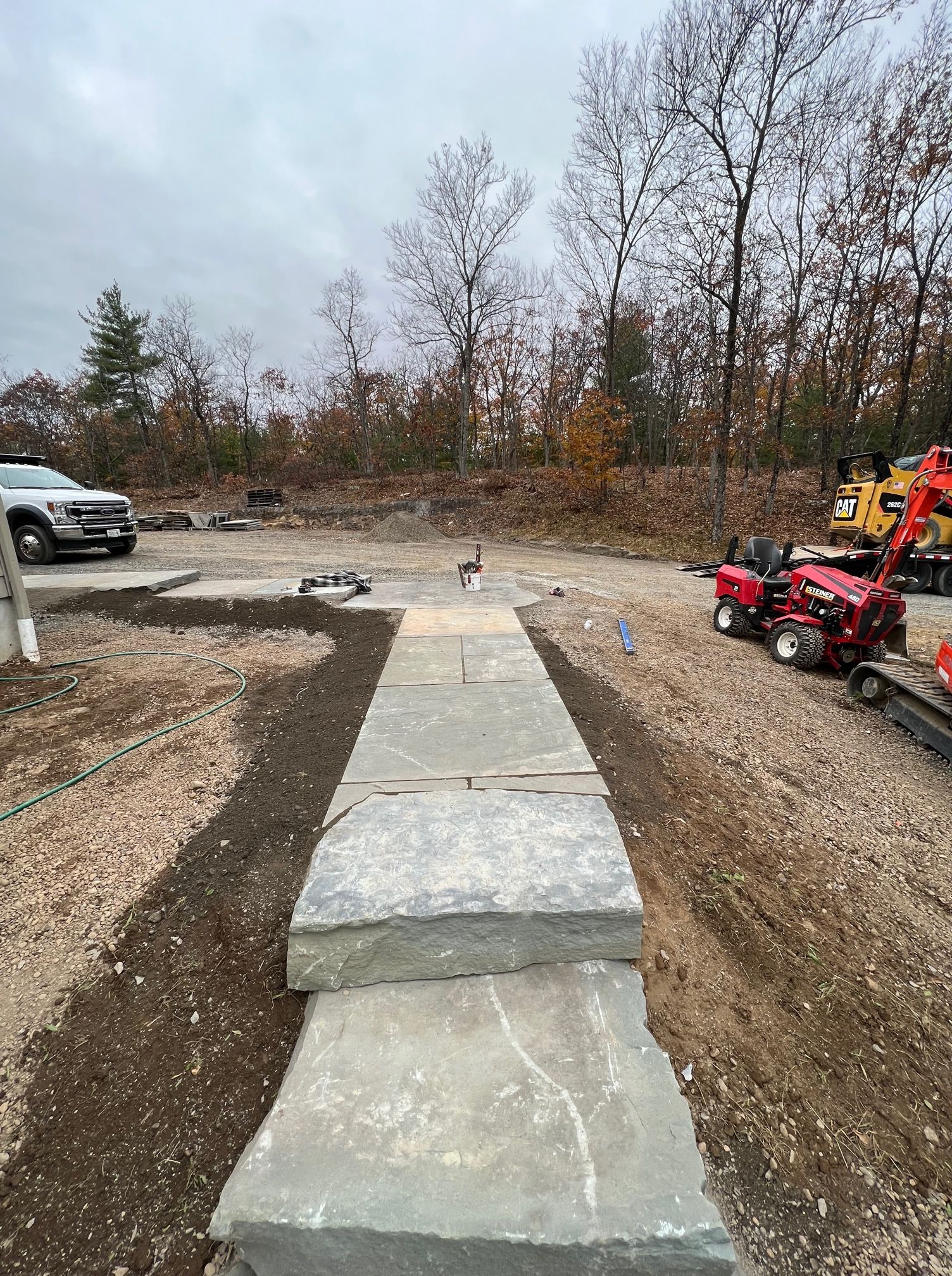 A tractor is parked in a dirt lot next to a stone walkway.