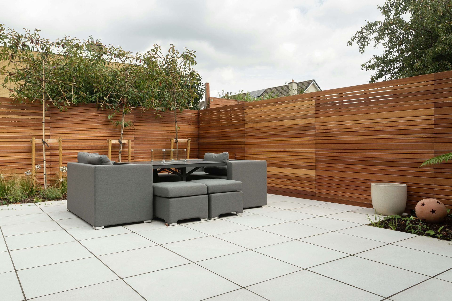 Outdoor patio with tiles and sectioned-off areas for plants and landscaping. 
