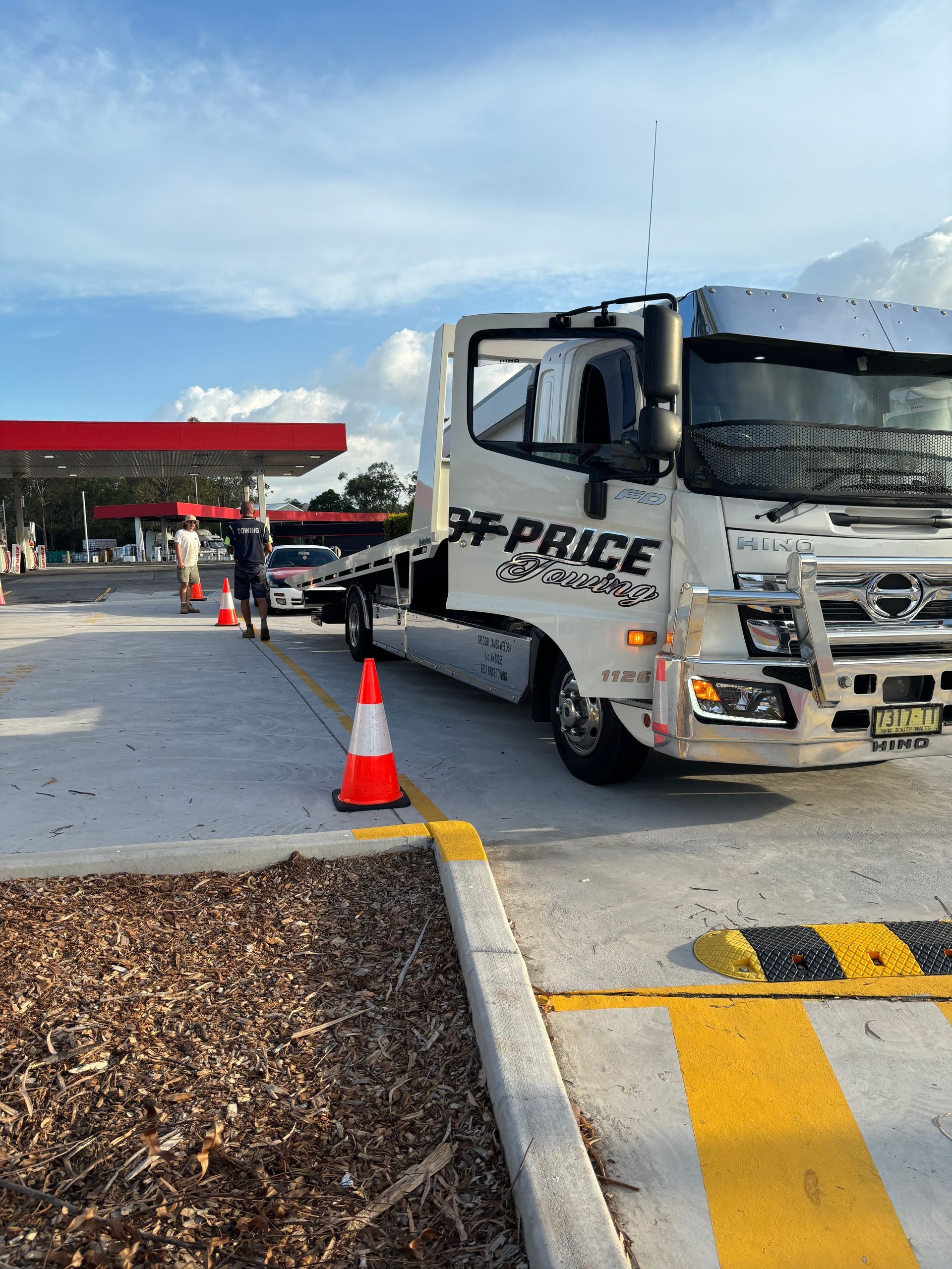 A best price towing tow truck is parked in a fuel station with cones around it while preparing to tow a small vehicle— Best Price Towing in Woongarrah, NSW