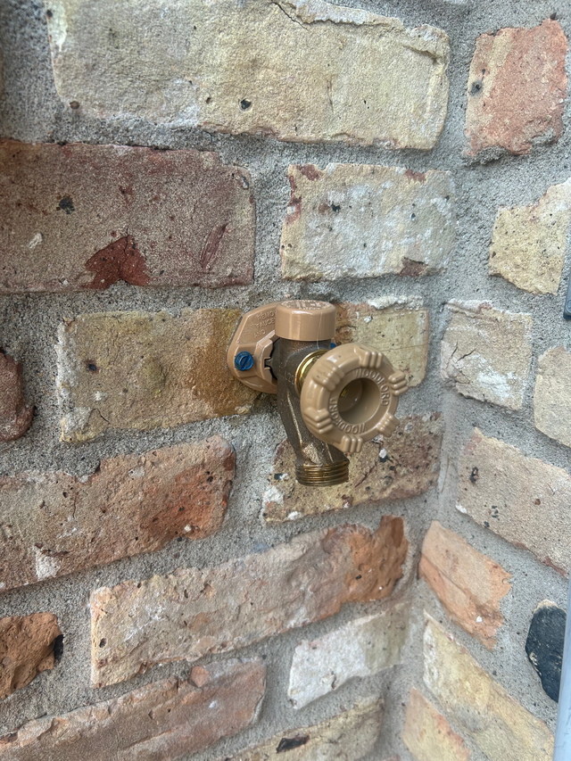 Brass outdoor hose bib mounted on a weathered brick wall.