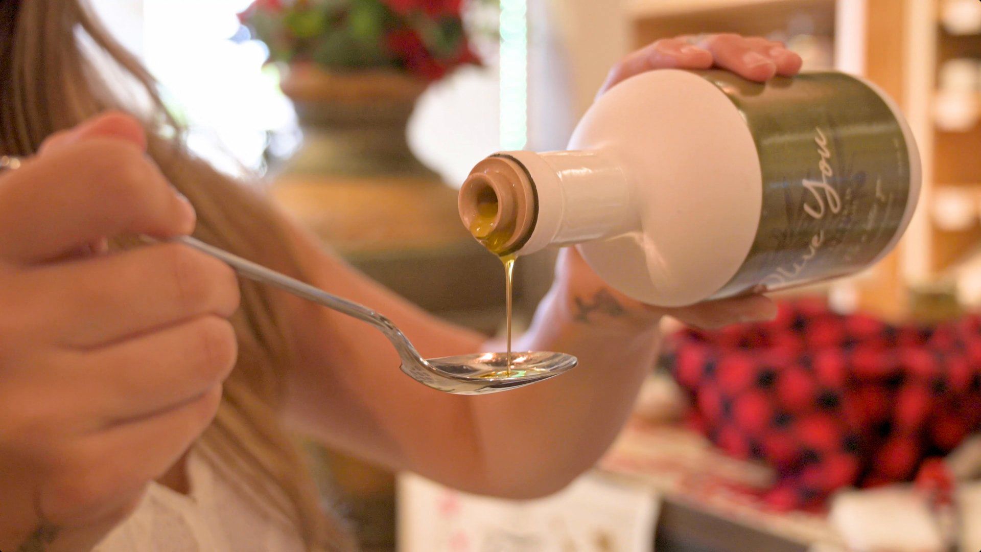 A woman is pouring olive oil into a spoon from a bottle.
