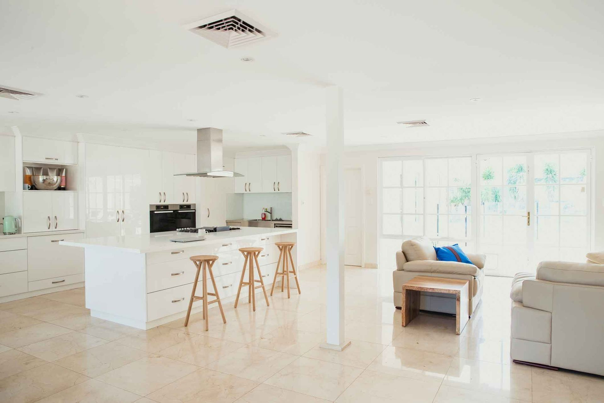 A Living Room With A Couch, Table, Stools And A Kitchen — Auslinc Building Services In Wingham, NSW