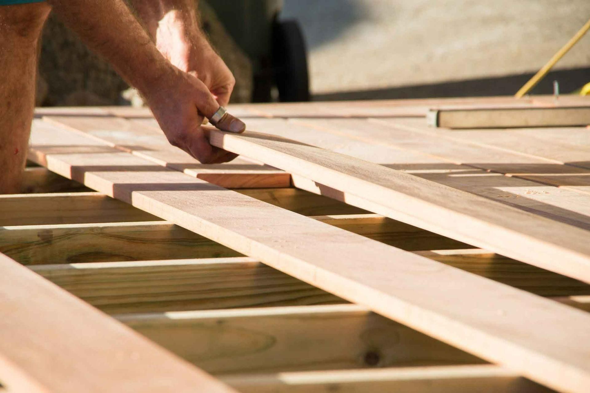 A Man Is Working On A Wooden Deck With His Hands — Auslinc Building Services In Wingham, NSW