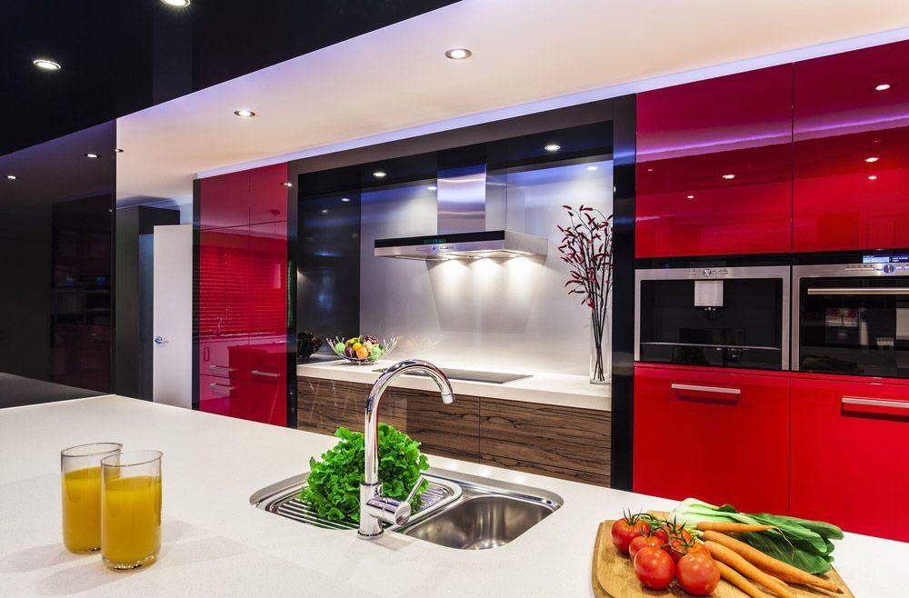 A Kitchen With Red Cabinets , A Sink , Two Glasses Of Orange Juice And Vegetables On The Counter — L.A.F Electrical P/L In Terrigal, NSW