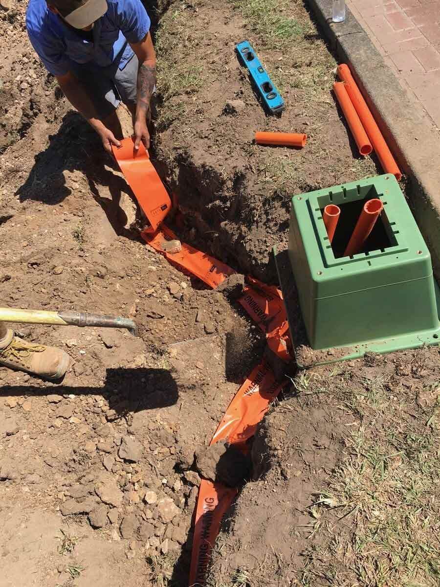 A Man Is Kneeling Down In The Dirt Next To A Green Box — L.A.F Electrical P/L In Avoca Beach, NSW