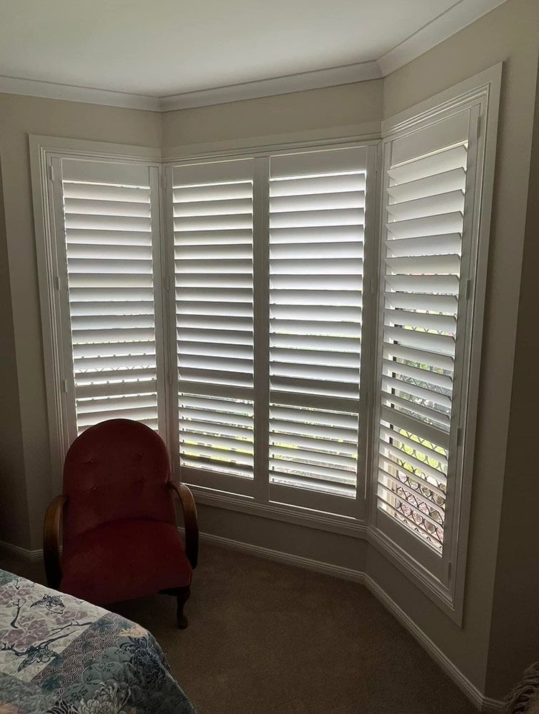 A Bedroom With White Shutters on the Windows and a Red Chair — Whitsunday Blinds & Security in Airlie Beach, QLD