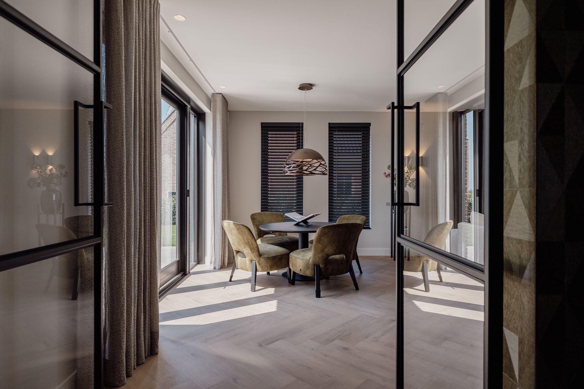 Moderne eetruimte met glazen deuren, een ronde tafel en beige stoelen in een lichte hal.