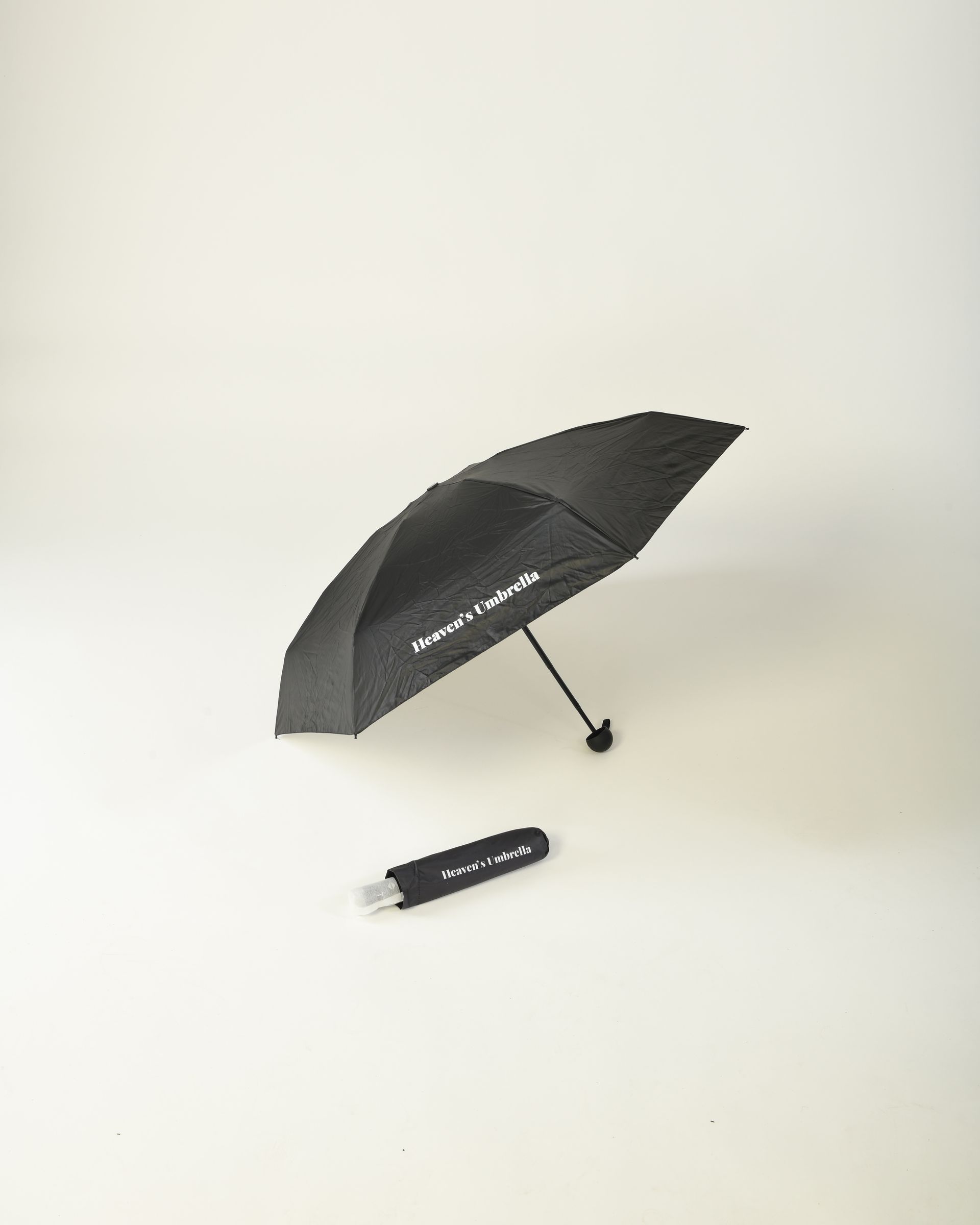 Black folded umbrella with handle and wrist strap on a white background