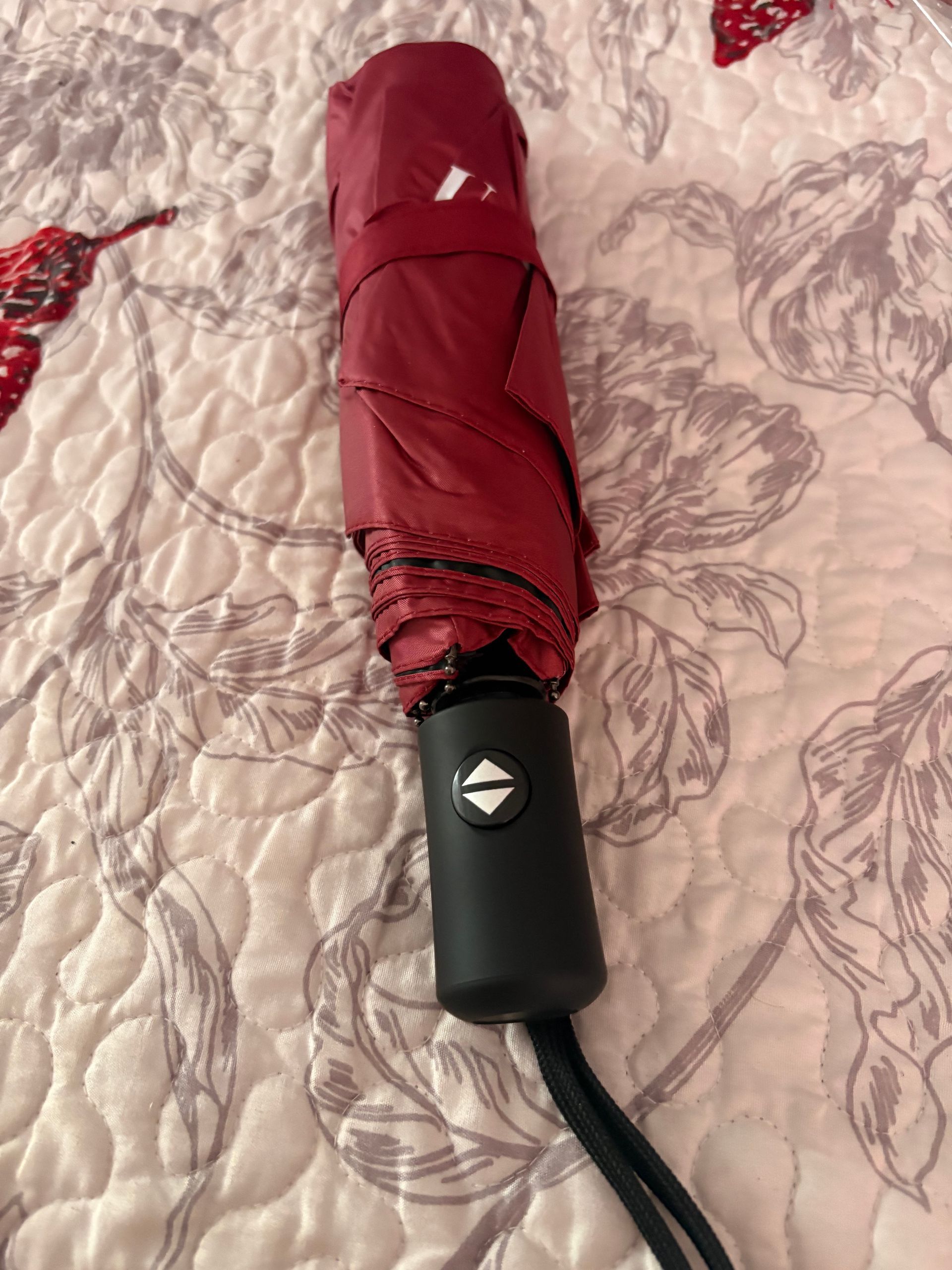 Closed red umbrella with black handle and wrist strap on a white background