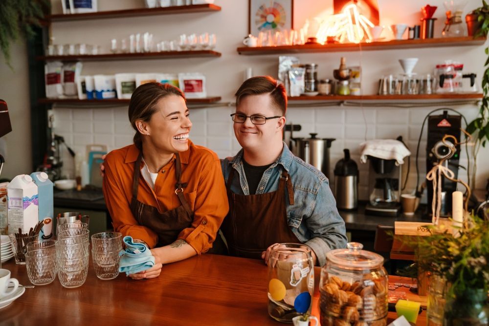 Mentally disabled man working at a coffee shop and smiling with his co-worker - First Aid in Mackay, QLD