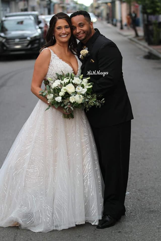 A bride and groom are posing for a picture on the street.