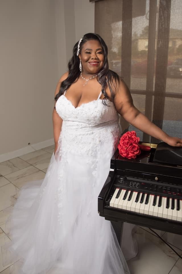 A woman in a wedding dress is standing next to a piano.