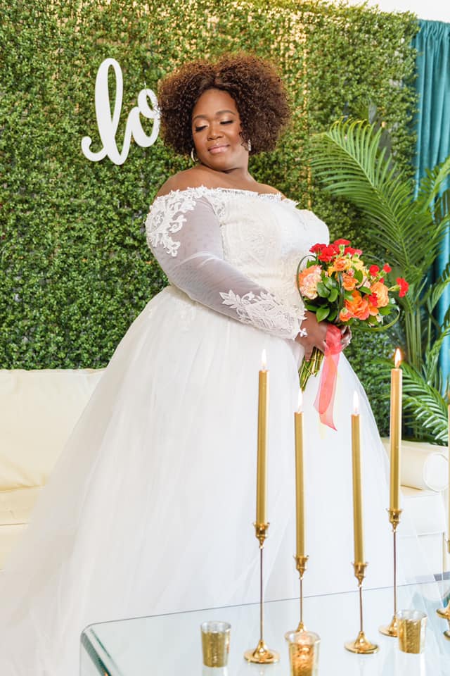 A plus size bride in a wedding dress is holding a bouquet of flowers and candles.