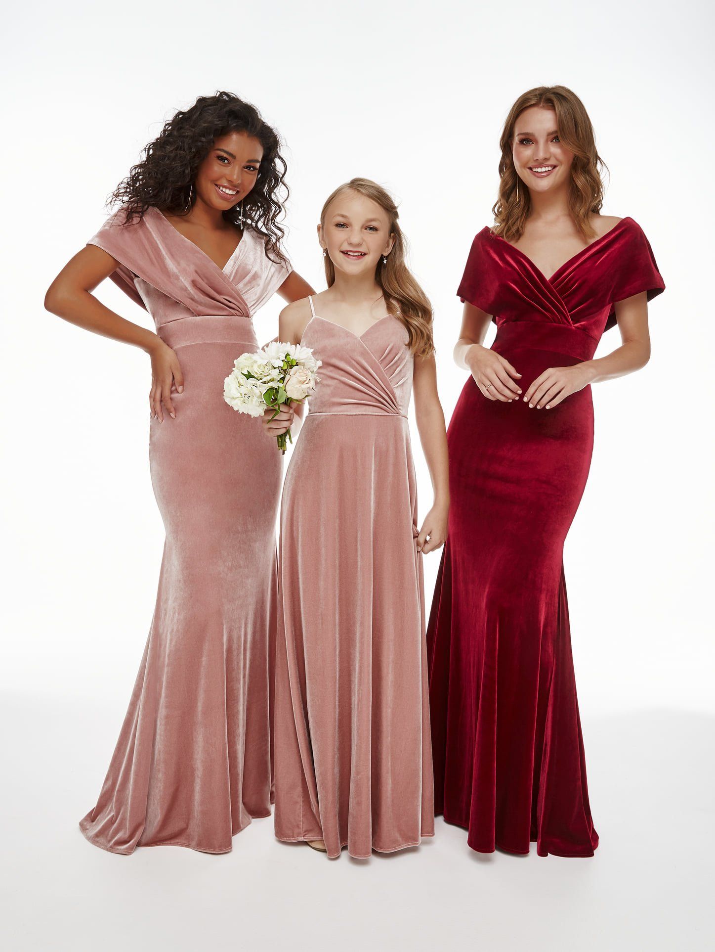 Three women are standing next to each other wearing velvet dresses.