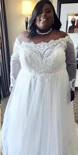 A plus size bride is standing in front of a mirror wearing a white wedding dress.