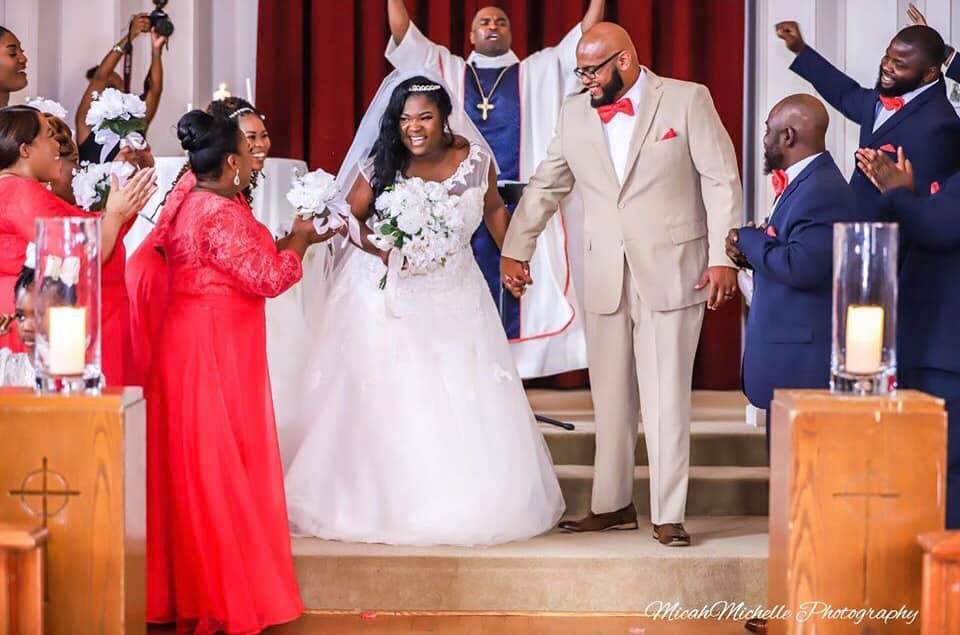 A bride and groom are walking down the aisle of a church holding hands.