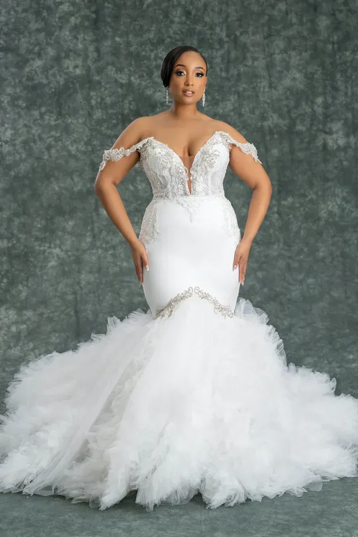 A woman in a white wedding dress is standing in front of a green background.