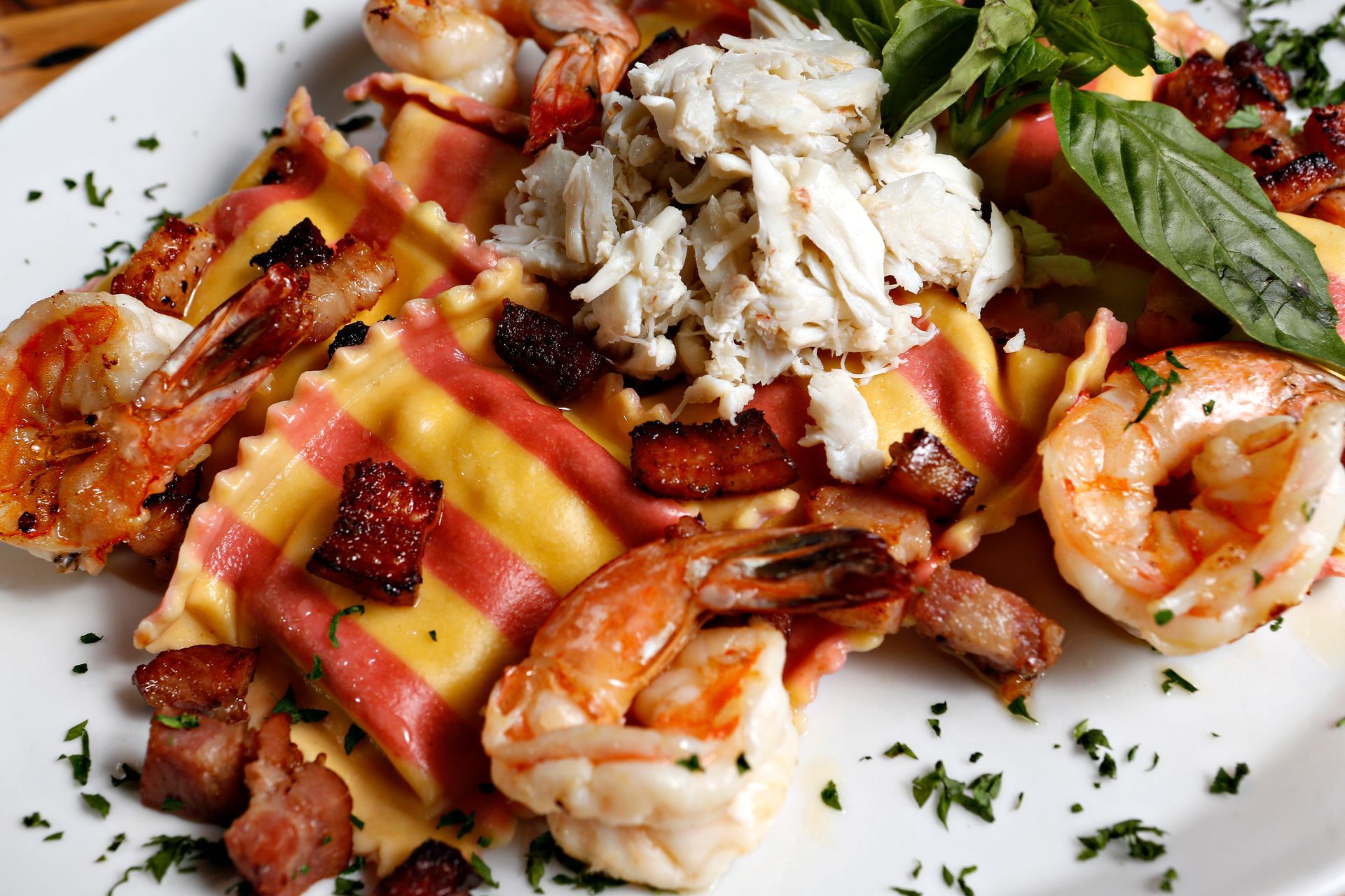 A white plate topped with ravioli shrimp and bacon