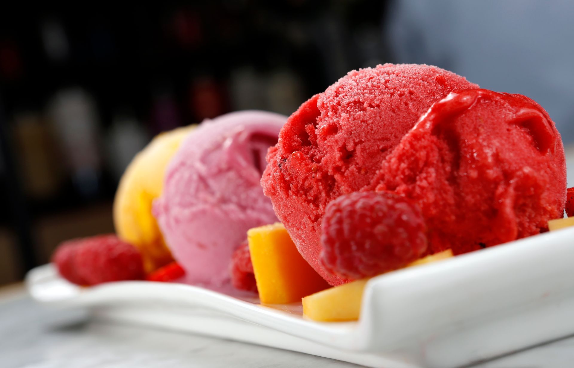 Three scoops of ice cream are on a white plate with fruit.
