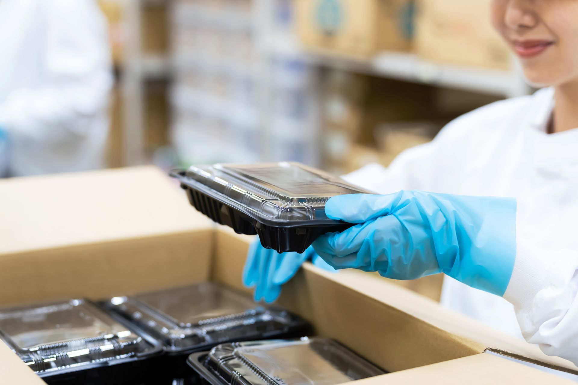 A woman wearing blue gloves is holding a plastic container in a box.