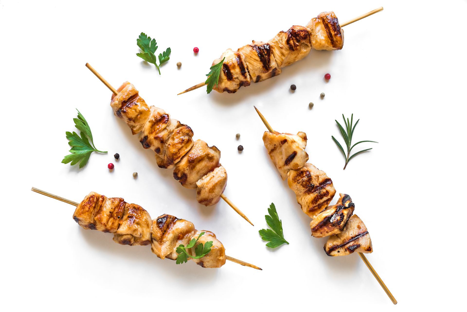 A close up of three chicken skewers on a white surface.