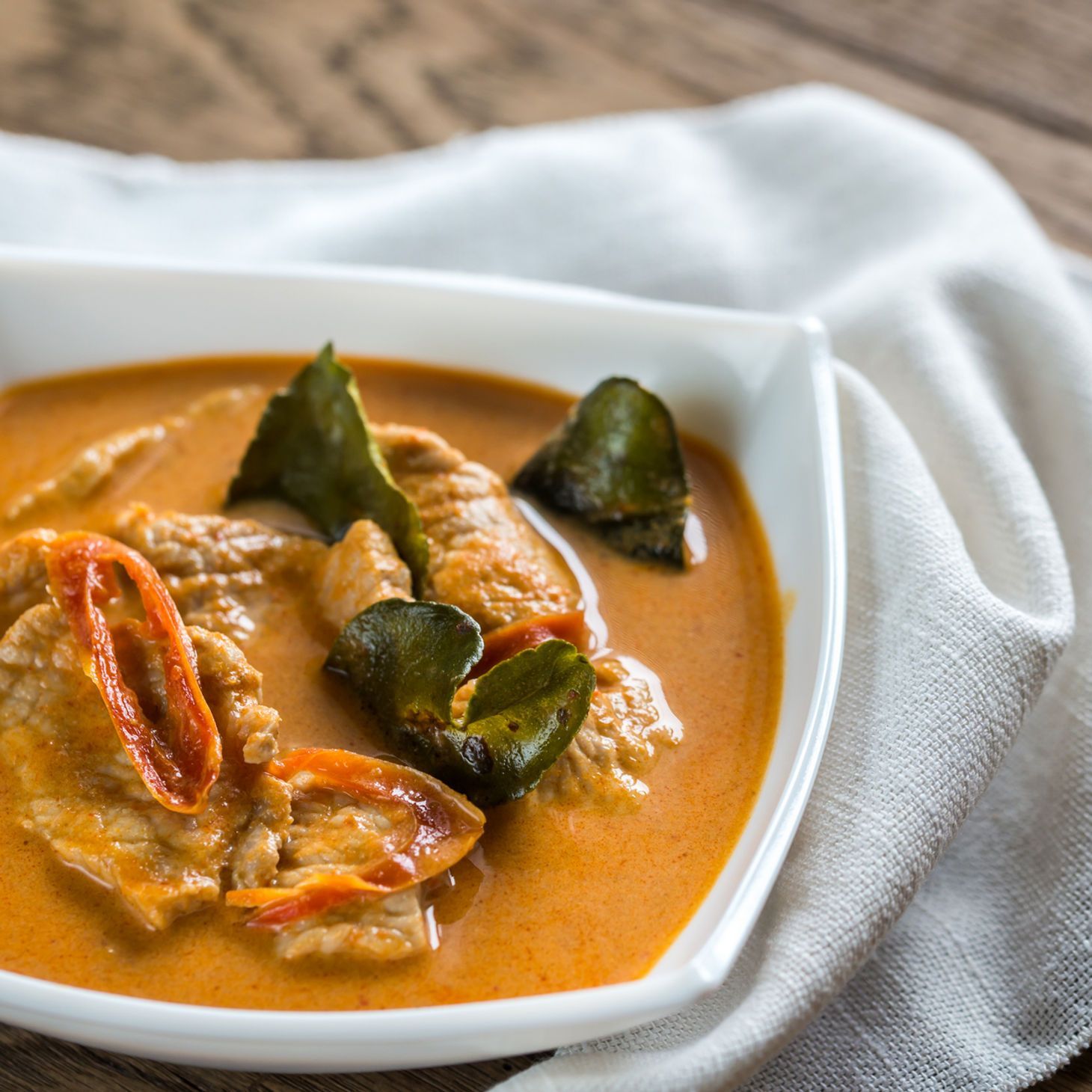 Creamy orange curry with shrimp and green garnishes in a white bowl on a cloth napkin