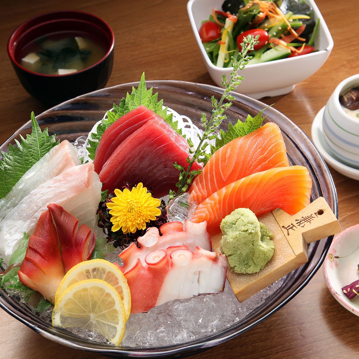 Sushi sashimi platter with salmon, tuna, octopus, lemon, wasabi, and miso soup on a wooden table