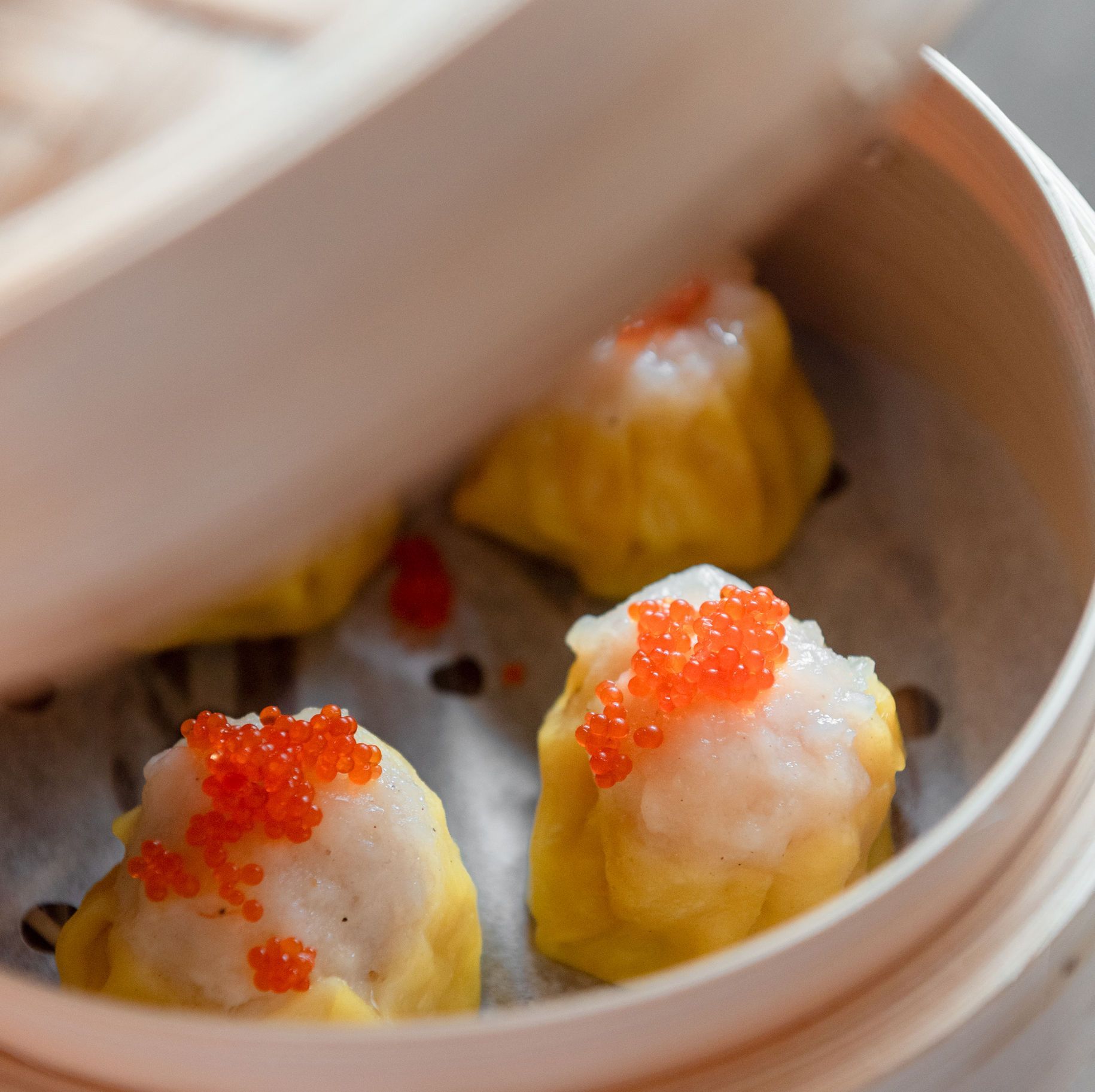 Steamed dumplings topped with orange roe in a bamboo basket