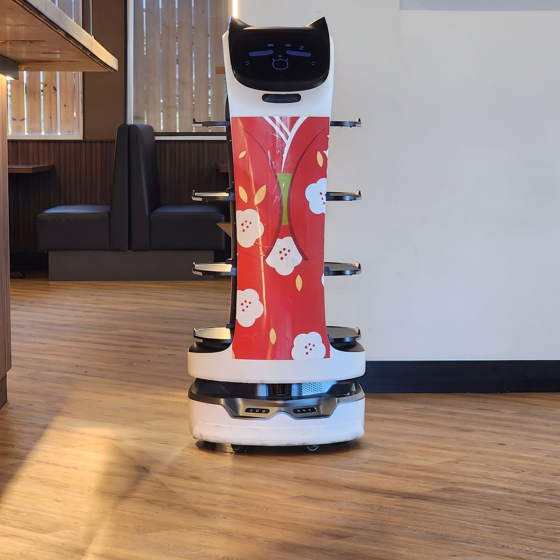 Small delivery robot with a red patterned body in a modern indoor lobby.